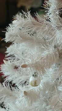 Vertical video. Woman decorating white Christmas tree with Christmas balls in cozy home.