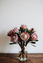 Obraz premium Interior design and home decor, bouquet of pink king protea flowers in a glass vase on a wooden table for lifestyle and botanical aesthetic concepts