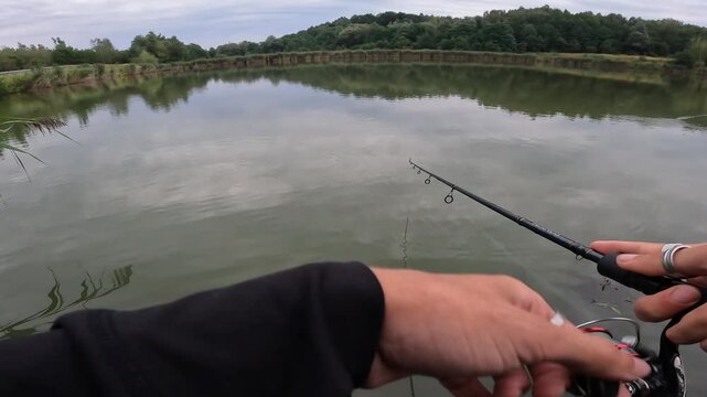 POV view of fisherman reeling spinning rod on a calm lake. Peaceful summer spin fishing for asp (Leuciscus aspius) and perch (Perca fluviatilis).