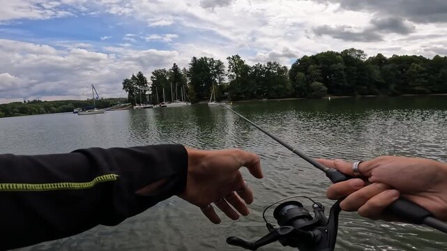 POV of angler casting spinning rod on a beautiful lake with sailboats. Summer recreational spin fishing for asp (Leuciscus aspius).
