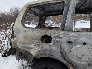 Burned out car wreck stands abandoned in snowy vegetation, ideal for fire damage, insurance and war concepts © PietFoto