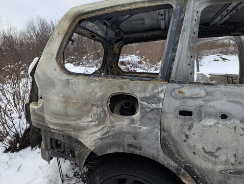 Burned out car wreck stands abandoned in snowy vegetation, ideal for fire damage, insurance and war concepts