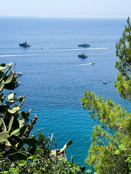 Scenic Sea View with Luxury Yachts Framed by Mediterranean Greenery. A high-angle vista overlooking the deep blue waters of the Mediterranean Sea, naturally framed by vibrant green pine trees and pric
