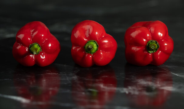 A close-up of red bell peppers reflected on a dark surface in the kitchen.