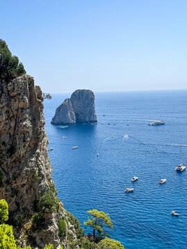 Scenic Coastline View of Faraglioni Rock Formations in Capri, Italy. A panoramic, high-angle view of the iconic Faraglioni sea stacks towering over the deep blue waters of the Mediterranean Sea. The s