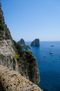 Scenic Coastline View of Faraglioni Rock Formations in Capri, Italy. A panoramic, high-angle view of the iconic Faraglioni sea stacks towering over the deep blue waters of the Mediterranean Sea. The s