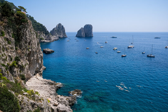 Scenic Coastline View of Faraglioni Rock Formations in Capri, Italy. A panoramic, high-angle view of the iconic Faraglioni sea stacks towering over the deep blue waters of the Mediterranean Sea. The s
