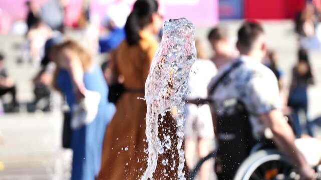 Water splashing from fountain in public square with blurred people cooling off