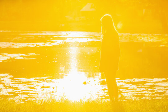 Teenage girl watching the sunrise by the water, symbolizing growing up, dreams and a bright future.. Copy space for text or design.