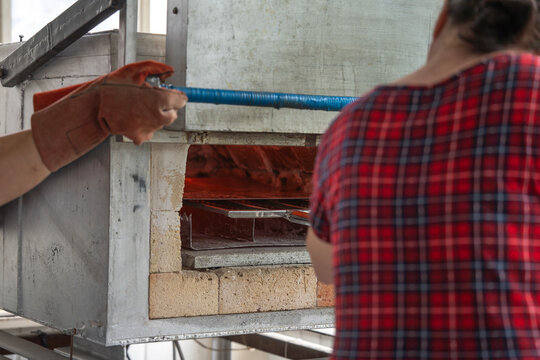 Artisan placing workpiece into hot muffle furnace for enamel firing, representing traditional crafts, metal enameling, and workshop production.