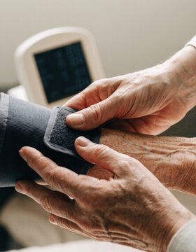 Detailed view of a caregiver gently placing a blood pressure cuff on the forearm of an elderly individual showcasing the importance of compassionate health monitoring and care techniques