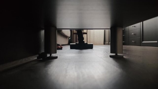 Cleaning under furniture with a vacuum cleaner at home in the evening