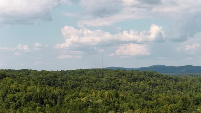 Aerial of dense forest and radio tower in Appalachian mountains in Huntsville Tennessee with rolling hills in the background and a partly cloudy sky