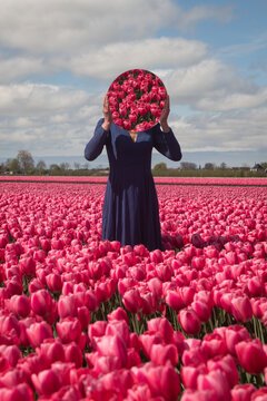 art portrait of woman in blue dress standing in field of pink tulips holding round mirror