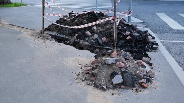 Road repair work creating pile of asphalt and debris next to warning tape
