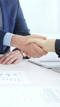 Business partners shaking hands at a meeting, celebrating successful negotiations and signing a contract, with documents, digital tablet, and smartphone on the table. Handshake close up