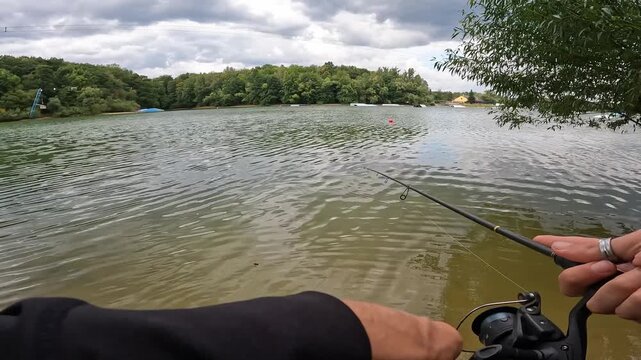POV of fisherman casting rod into a calm forest lake, targeting asp (Aspius aspius). Outdoor recreation concept.