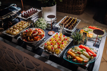 Fototapeta premium Assorted gourmet food display featuring colorful appetizers, sushi, and desserts arranged on a buffet table with decorative elements in a modern setting