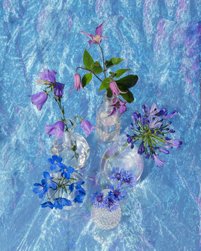 art photo of five glass vases with flowers on shiny fabric in blue and purple colors