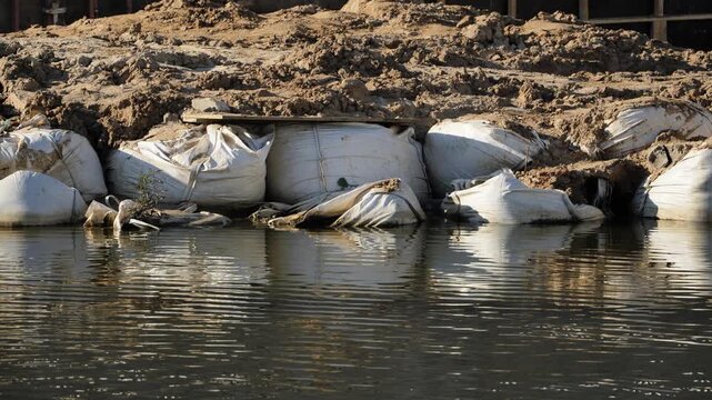 Sandbags holding back rising floodwaters along a temporary river bank during a disaster