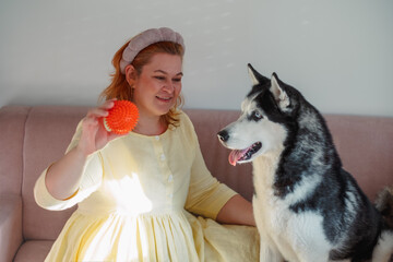 Woman holding an orange ball in front of a husky © iwavephoto