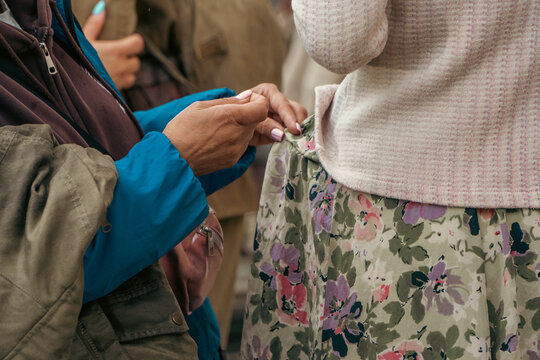 A woman carefully uses a needle and thread to repair and adjust the waistband of another woman's floral patterned dress during an outdoor event.