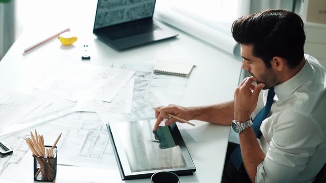 Architect engineer using laptop planning house design at office while sitting at meeting table with blueprint and equipment scatter around.Skilled civil engineer working at blueprint. Alimentation.