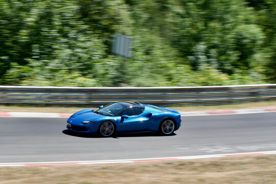 Blue Ferrari 296 GTS driving on the Nurburgring motor racing track in Germany.