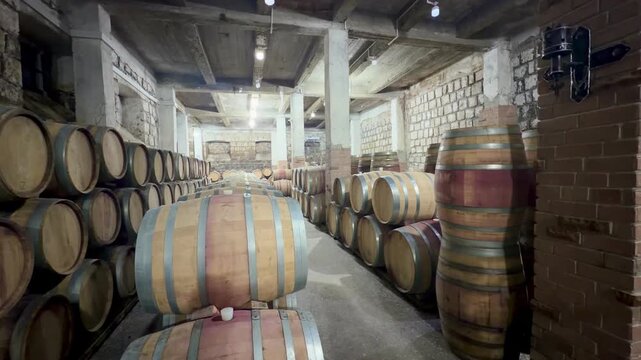 Interior of a wine cellar featuring rows of wooden barrels stacked against stone walls, highlighting the aging process in a rustic setting