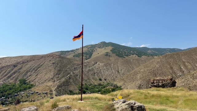 Armenian flag flutters on a hill, surrounded by mountains and greenery, capturing the scenic beauty of the Bjni Fortress area in Armenia