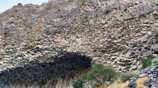 Garni, Armenia - August 26, 2026: Unique geological formation of hexagonal basalt columns captured under a clear blue sky with surrounding vegetation visible