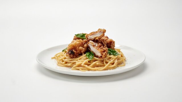 Linguine with fried chicken pieces served on a white plate with fresh herbs on a light surface