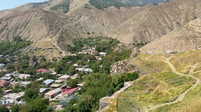 Scenic panorama of Bjni Fortress, highlighting the village and lush greenery in the valley, framed by rugged mountains and clear blue skies