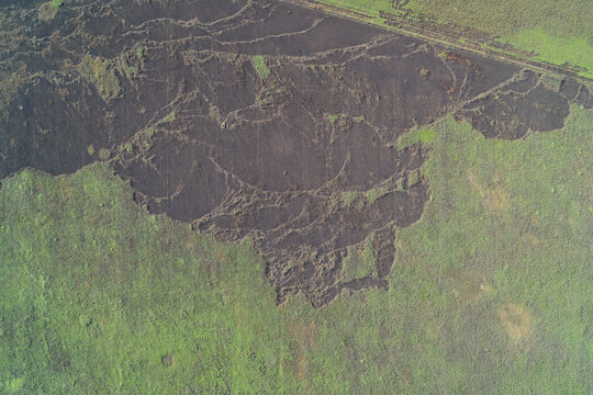 Large burnt patch with black ash on green agricultural field from missile strike, top down drone shot