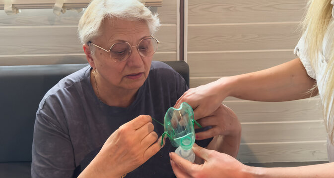 Nurse assisting an elderly woman with an incentive spirometer. Senior patient doing respiratory therapy in a rehabilitation clinic. Healthcare and COPD treatment concept