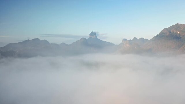 Thailand, Khao Sok National Park aerial landscape, towering limestone mountains karst and lush tropical rainforest emerge from a thick blanket of morning fog. Aerial drone fly through mist and clouds