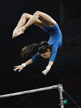 Female gymnast performing dynamic flight element on uneven bars at professional gymnastics tournament