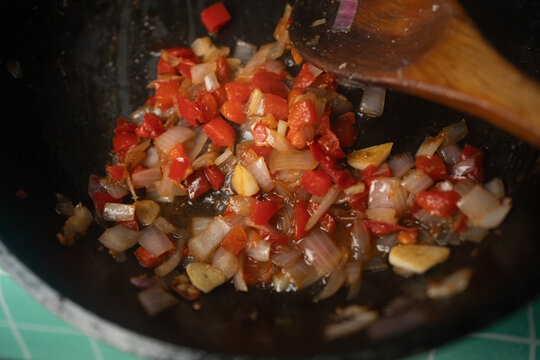 Selective Focus Cooking Sofrito with Wooden Spatula in Frying Pan, Macro Focus on Saut&eacute;ing Diced Onions Red Peppers and Garlic in Pan