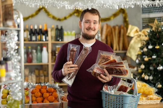 Man in a sweater chooses ham and dried sausages in a supermarket. Customer chooses sliced meat delicacies against the background of a Christmas tree