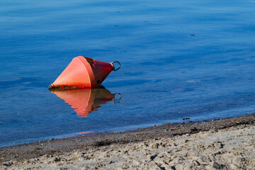 Damaged orange buoy floating near sandy shore in calm blue water © Holger
