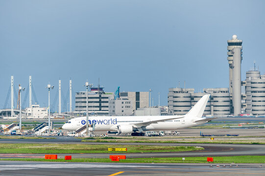 駐機場にたたずむ白い機体の旅客機と遠景の管制塔/White Airliner Parked at the Airport with Control Tower in the Distance