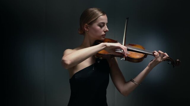 Young adult Caucasian woman playing violin with bow in studio. Footage is ideal for classical music concert promotions, artistic performance videos, and music education advertisements