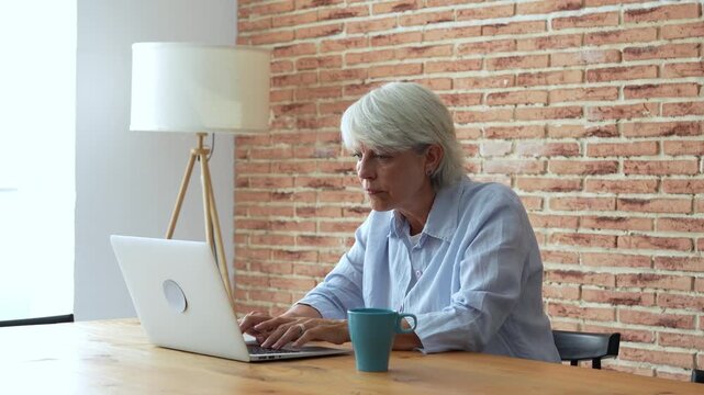 Mature woman working on her laptop from a home office, experiencing stress and fatigue, stopping to rub her temples and think while feeling the pressure of a deadline or a complex problem