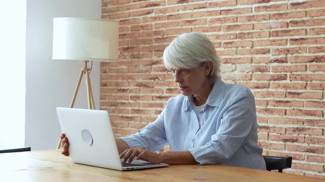 Upset elderly businesswoman experiencing computer problems while working remotely, feeling stressed and tired from a difficult online task, and showing signs of frustration and headache