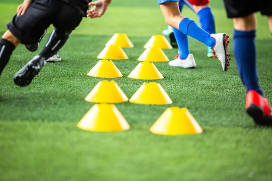 Selective focus to soccer cones with blurry kid legs training soccer on artificial turf grass.