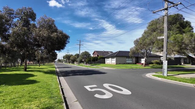 Quiet residential street in Altona Meadows featuring a painted 50 km/h road speed limit mark, wooden utility poles,&nbsp;brick homes,&nbsp;in Melbourne, Victoria, Australia.