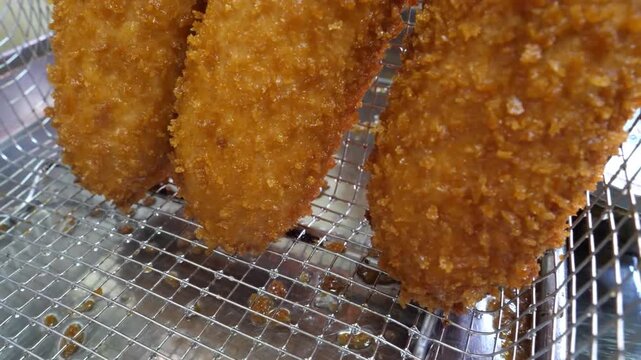 A detailed, close-up shot focusing on multiple freshly deep-fried, ultra-crispy Korean-style corn dogs on wooden skewers. The camera captures the golden-brown panko breadcrumb crust glistening with oi