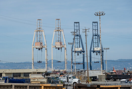 Port Cranes-Large industrial shipping cranes stand tall against a clear blue sky near a concrete harbor pier.