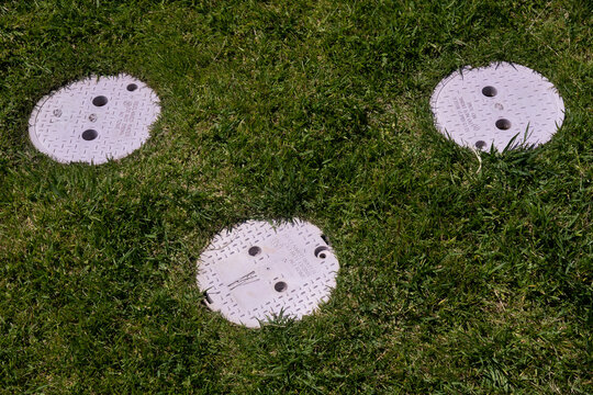 Reclaimed Water Caps-Three purple utility covers marked for reclaimed water are embedded in a lush patch of green grass.