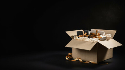 Fototapeta premium A cardboard box overflowing with beautifully wrapped gifts and golden ribbon, set against a dark background.